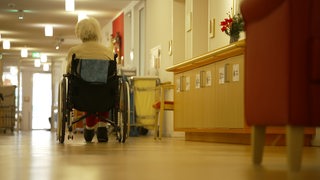 Eine Seniorin rollt mit ihrem Rollstuhl durch den Flur einer Pflegeeinrichtung.