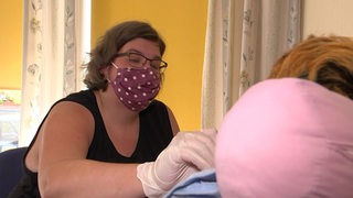 Pflegerin Stefanie Lienemann, mit Mundschutz und Handschuhen, kümmert sich um eine Person im Rollstuhl.