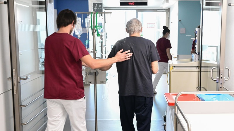 Ein Pfleger begleitet einen Patienten durch ein Krankenhaus.