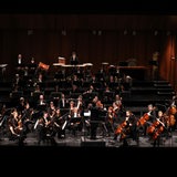 Musiker sitzen als Orchester mit ihren Instrumenten auf einer erleuchteten Bühne.