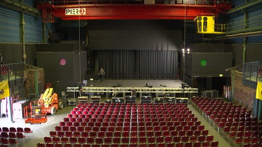 Ein leerer Konzertsaal. Vor der bühne stehen viele rote Stühle aufgereiht.