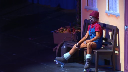 Ein Mädchen mit Rollschuhen und Kostüm sitzt während einer Theateraufführung auf einer Bank.