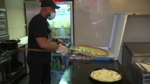 Ein Mitarbeiter in einer Pizzeria schiebt eine frische Pizza in einen Pizzakarton zum Transport. 