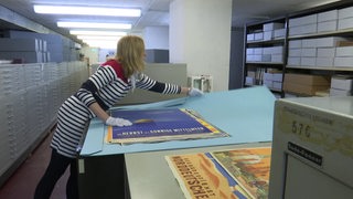 Die Archivarin Brigitta Nimz zeigt die antiken Plakate, die im Keller des Bremer Staatsarchiv aufbewahrt werden. 