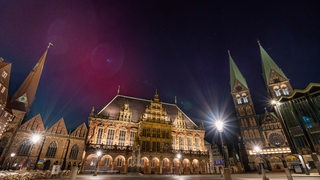 Der Bremer Marktplatz bei Nacht, über dem Rathaus leuchten Polarlichter.