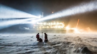 Forscher stehen vor dem Forschungseisbrecher Polarstern im Eis.