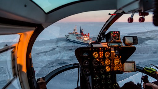 Das Forschungsschiff Polarstern ist aus dem Cockpit eines Hubschraubers aus der Luft im Eis zu sehen.