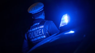 Ein Polizist steht om Dunkeln neben einem Polizeifahrzeug 