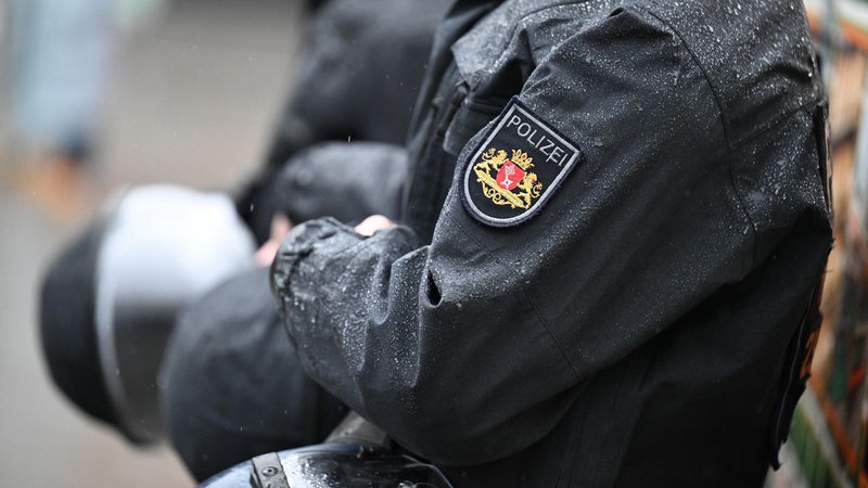 Polizisten im Einsatz bei einer Demonstration, Regentropfen sind auf den Uniformjacken zu sehen, die Helme sind in den Händen.