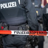 Polizisten stehen hinter einem Polizei-Flatterband.