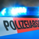 Eine Polizeiabsperrung führt vor einem Blaulicht entlang.