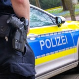 Ein Polizist mit einer Waffe am Gürtel steht vor einem Polizeiauto.