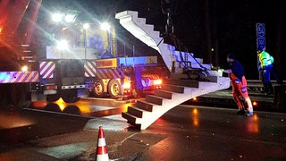 Eine Treppe wird nachts mit einem Kran von der Autobahn gehoben