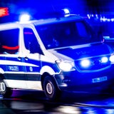 Ein Polizei-Kleinbus fährt nachts mit Blaulicht über eine Straße.
