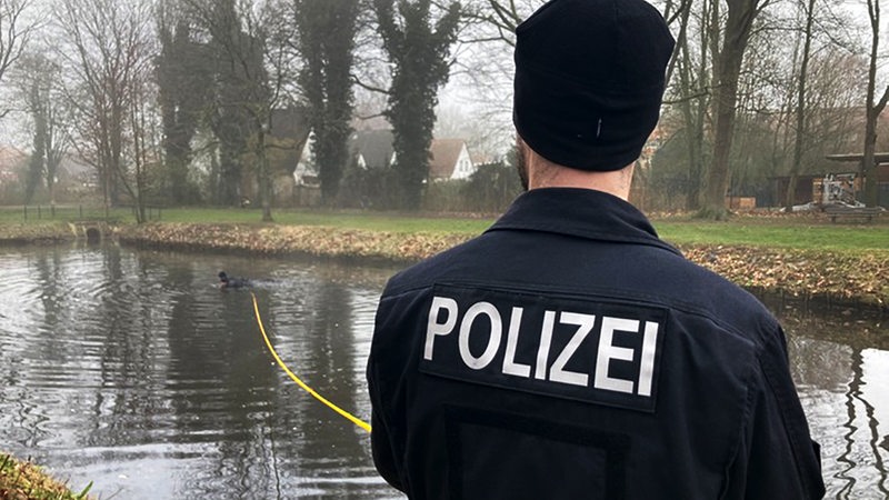 Ein Polizeibeamter steht mit einer Rettungsleine am Ufer eines Flusses