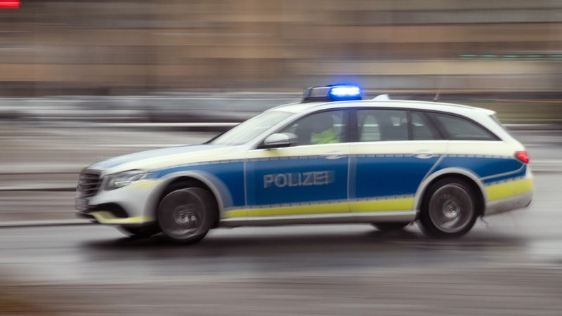 Ein Polizeiwagen fährt mit Blaulicht auf einer Straße.