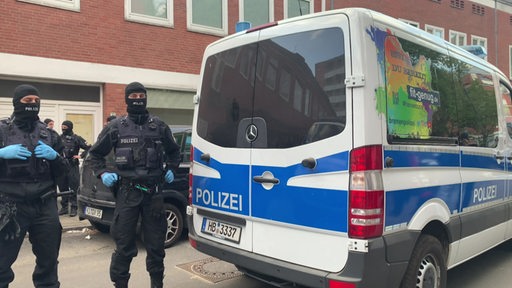 Zwei Polizisten stehen bei einem Einsatz neben dem Einsatzwagen