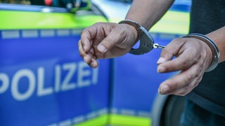 Ein Mann steht in Handschellen vor einem Polizeiwagen.