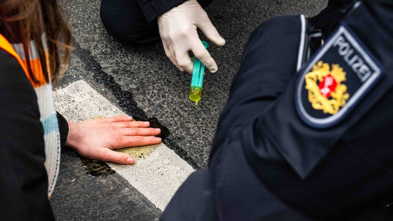 Einsatzkräfte der Polizei lösen den Klebstoff, mit dem sich eine Aktivistin der Letzten Generation am Rembertiring festgeklebt hat. 