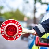 Der Arm einer Polizistin vor einem Polizeiauto mit Polizeikelle an einer Straße