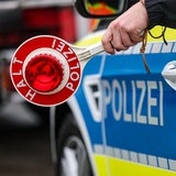 Ein Polizist hält eine Polizeikelle aus einem Fahrzeug für eine Kontrolle auf einem Parkplatz