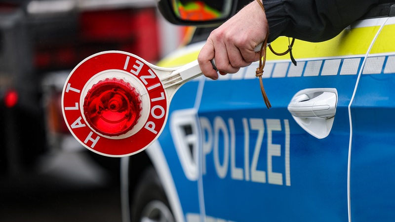 Ein Polizist hält eine Polizeikelle aus einem Fahrzeug für eine Kontrolle auf einem Parkplatz