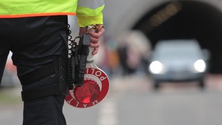 Ein Polizist steht mit einer Kelle vor einem Tunnel.