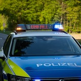 Ein Polizeiauto steht auf einer Landstraße. Auf einer Leuchttafel auf dem Dach des Autos steht "Unfall".