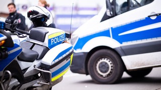 Ein Polizeimotorrad und ein Streifenwagen stehen auf einer Straße.