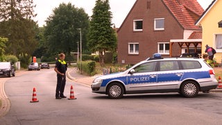 Ein Polizeiauto steht an einer Kreuzung, daneben eine Polizistin.