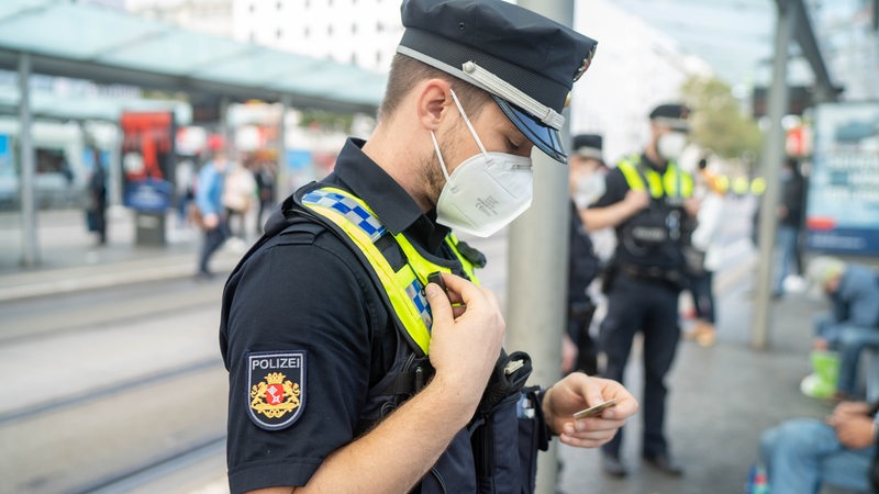 Ein Polizist mit Maske am Bahnhof guckt auf einen Ausweis