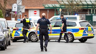 Die Polizei sperrt die Friedrichstraße in Nienburg. Zu sehen sind drei Polizisten, zwei Polizeiautos und ein rot-weißes Absperrband.