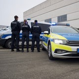 Drei Polizisten von hinten vor und neben einem Polizeiwagen