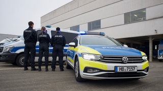 Drei Polizisten von hinten vor und neben einem Polizeiwagen