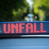 Ein Einsatzfahrzeug der Polizei steht mit Blaulicht und dem Schriftzug Unfall im Display an einem Unfallort.