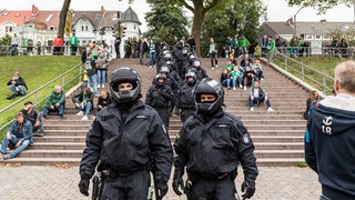 Polizisten stehen in der Nähe des Weser-Stadions. Im Hintergrund sind Werder-Fans zu sehen.