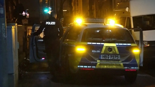 Ein Polizeibeamter steigt in ein Polizeiauto mit leuchtenden Warnblinkern.