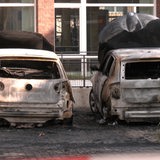Vor einer Polizeiwache stehen zwei ausgebrannte Zivilfahrzeuge.