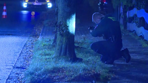 Ein Polizist fotografiert an einem Tatort einen Baum.