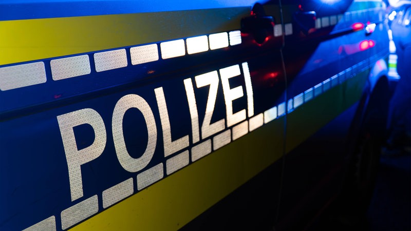 Auf einer Seitentür eines Autos steht "Polizei". In der Dunkelheit ist noch Blaulicht zu sehen.