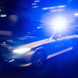 Ein Polizeifahrzeug fährt im Rahmen eines Fototermins mit Blaulicht an einem Gebäude vorbei.