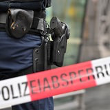 Die Waffe eines Bundespolizisten ist in seinem Holster zu sehen, davor Absperrband