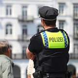 Ein Polizist beobachtet das Geschehen in einer Innenstadt. Er steht mit dem Rücken zum Fotografen und trägt Uniform.