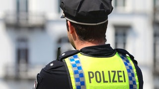 Ein Polizist beobachtet das Geschehen in einer Innenstadt. Er steht mit dem Rücken zum Fotografen und trägt Uniform.