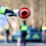 Ein Polizist hält eine rote Kelle in der Hand, um ein Auto anzuhalten. 