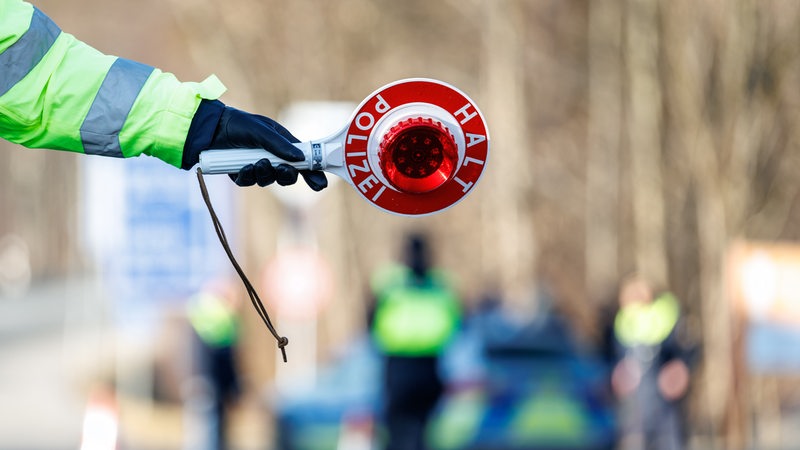 Ein Polizist hält eine rote Kelle in der Hand, um ein Auto anzuhalten. 