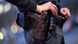 Die Hand eines Polizisten liegt auf seiner Waffe, die im Holster steckt.