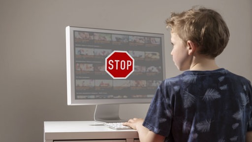 Ein Junge schaut auf einem Bildschirm, auf dem ein großes Stop-Schild vor einer Pornoseite zu sehen ist.