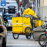 Ein Briefträger fährt mit seinem Fahrrad eine Straße entlang.
