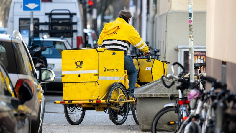 Ein Briefträger fährt mit seinem Fahrrad eine Straße entlang.